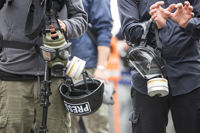 image or two male reporters holding gas masks, a tripod and a helmet with a “PRESS" imprint.